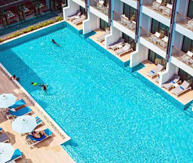 En utomhuspool med solstolar och parasoller vid sidan om samt byggnader med terrasser. (AI-genererad text)