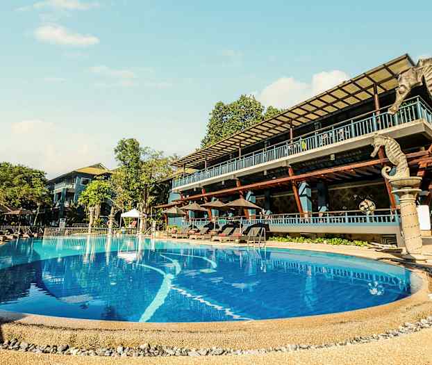 Utomhusbassäng vid ett hotell med solstolar och omgivande träd. (AI-genererad text)