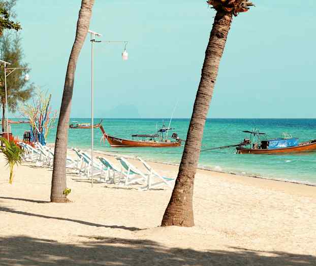 Strand med palmer, solsängar och traditionella träbåtar i havet. (AI-genererad text)