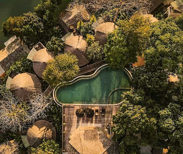 Flygfoto av flera runt formade hus omgivna av frodig grönska, vid sidan av en oregelbunden pool och en träterrass. (AI-genererad text)