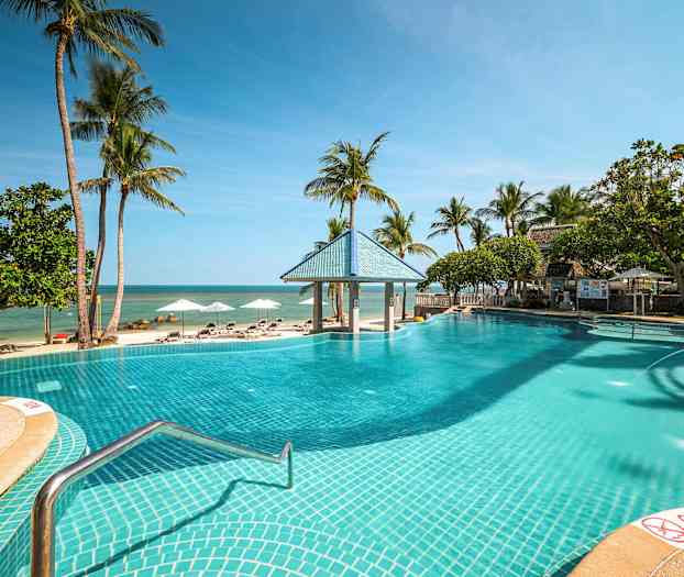 En utomhuspool vid en sandstrand med palmer och solsängar. (AI-genererad text)