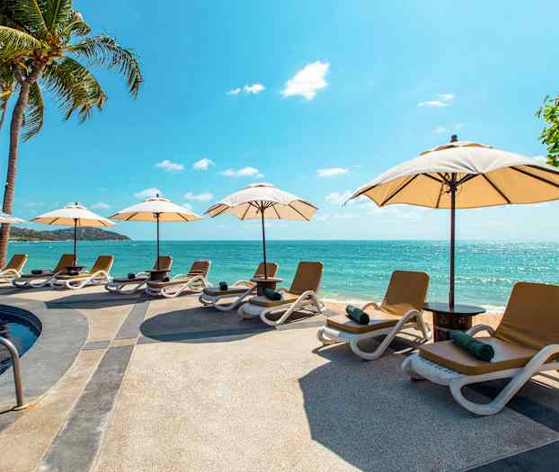 Strand med solstolar och parasoller vid en pool nära havet. (AI-genererad text)