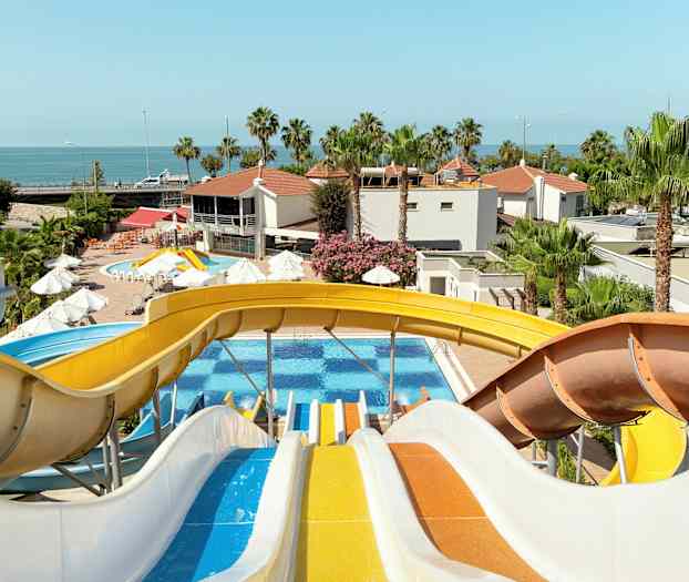 Flera färgglada vattenrutschkanor leder ner mot en pool med palmer och byggnader i bakgrunden. (AI-genererad text)