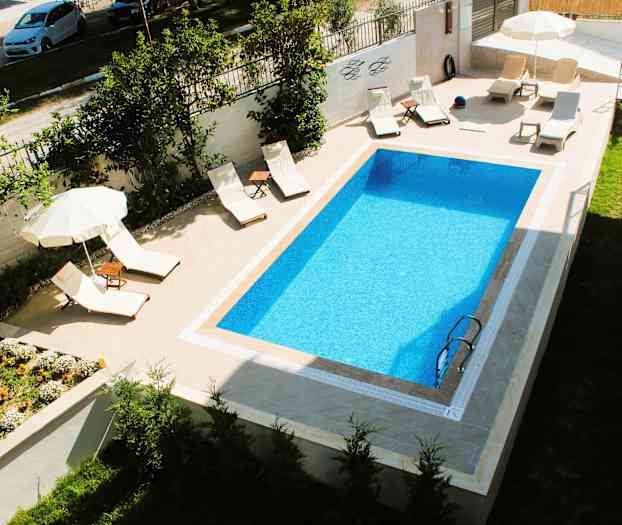 En rektangulär pool med solstolar och parasoller vid sidan. (AI-genererad text)