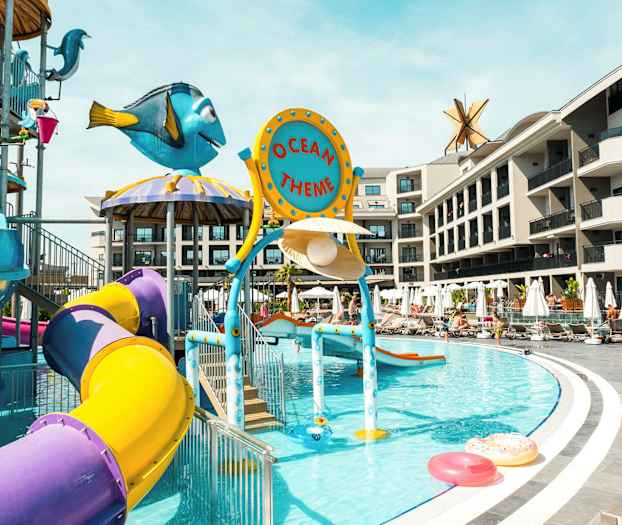 Bild av en vattenlekplats med färgglada rutschkanor och temadekorationer vid en pool. I bakgrunden syns hotellbyggnader. (AI-genererad text)