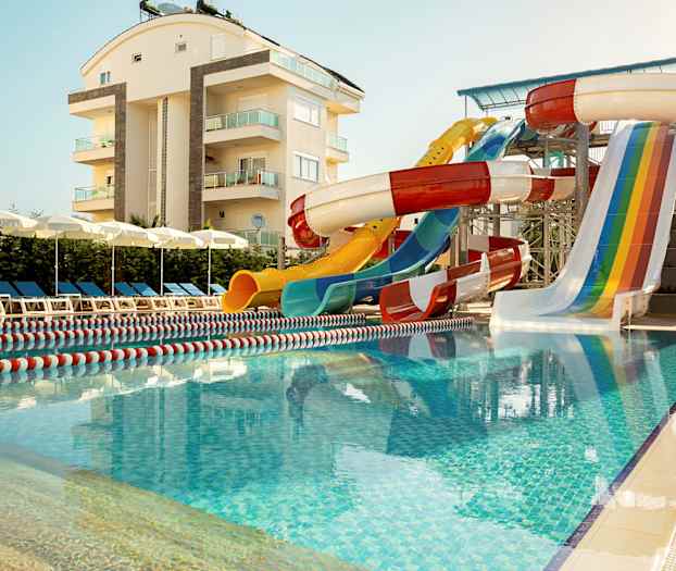 Utomhuspool med vattenrutschbanor och solstolar i närheten av en lägenhetsbyggnad. (AI-genererad text)