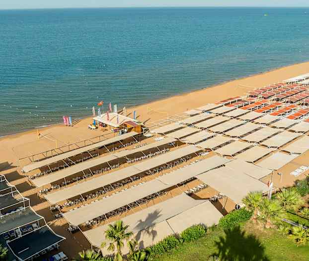 En sandstrand med solskydd under vilka solstolar är placerade. (AI-genererad text)