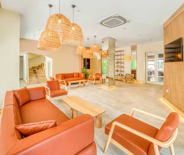 En ljus lounge med bruna soffor och fåtöljer, träbord och hängande lampor av rotting. (AI-genererad text)