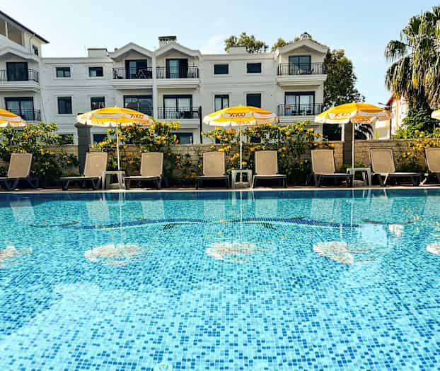 En pool med solstolar och gula parasoller framför ett flerbostadshus. (AI-genererad text)