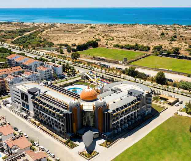 Hotell med unik arkitektur nära havet, omgiven av vegetation och grönområden. (AI-genererad text)