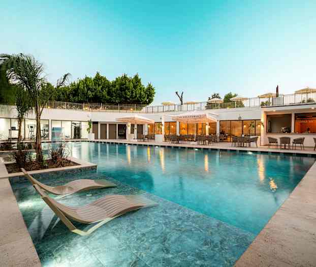 Utomhuspool med solstolar och restaurang i bakgrunden. (AI-genererad text)