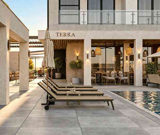 Ett hotellområde med solstolar vid en pool, omgivna av en restaurang med bord och stolar under tak med lampor. (AI-genererad text)