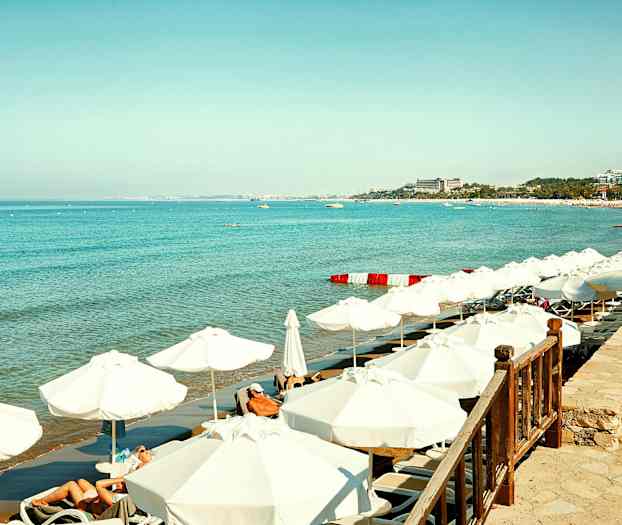 Vit sandstrand med solstolar och parasoller vid klarblått hav. (AI-genererad text)