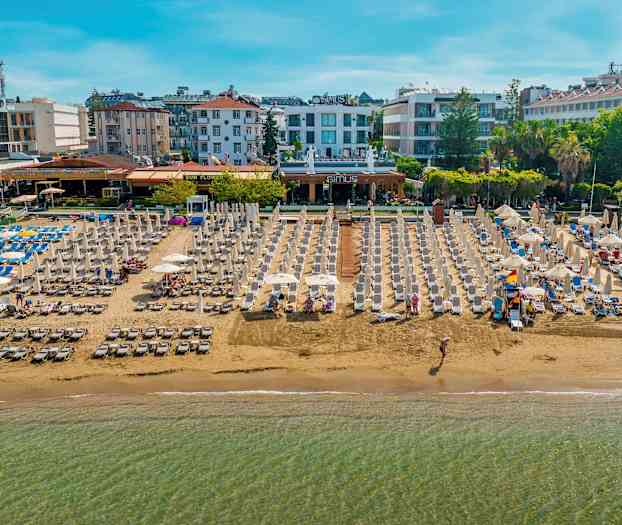 Strand med solsängar och parasoller, omgiven av hotell och byggnader. (AI-genererad text)