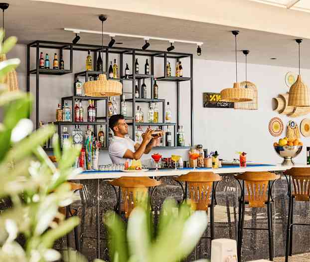 En bar med hyllor fyllda med flaskor och tre trästolar framför. (AI-genererad text)