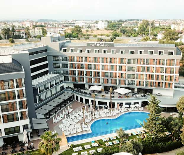 Flygfoto över hotellbyggnad med poolområde och solstolar framför. (AI-genererad text)