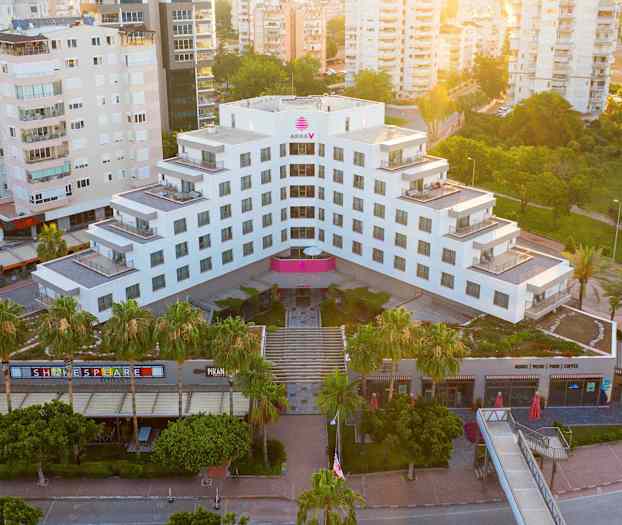 Ett modernt hotell omgivet av grönska och andra byggnader, sett från ovan. (AI-genererad text)