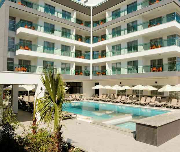 Hotellbyggnad med moderna balkonger och en pool omgiven av solstolar och parasoller. (AI-genererad text)