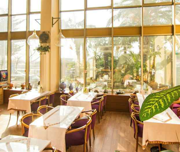 Bild av ett ljust café med stora glasfönster, dekorerat med bord och stolar med lila dynor. (AI-genererad text)