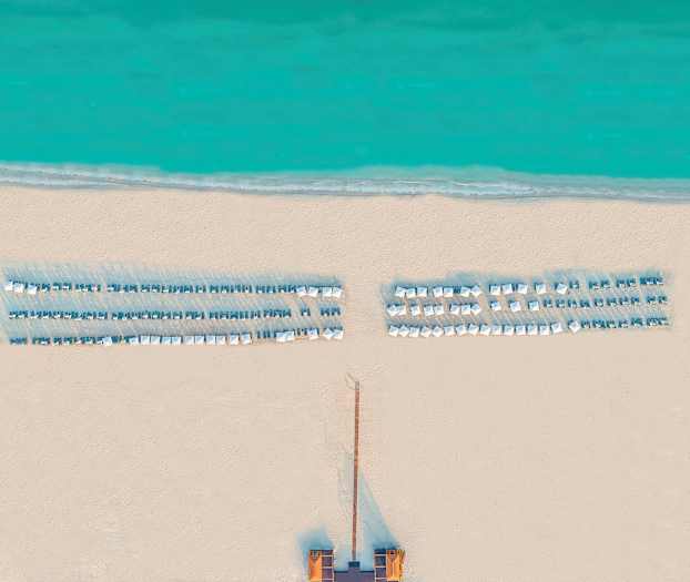 Flygfoto av en strand med solstolar och parasoller vid havet. (AI-genererad text)