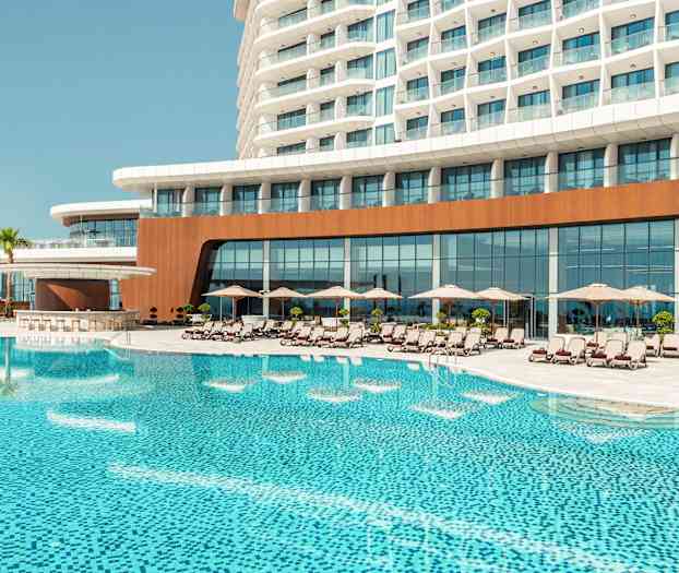 Ett hotellkomplex med en stor pool framför, omgivet av solstolar och parasoller. (AI-genererad text)