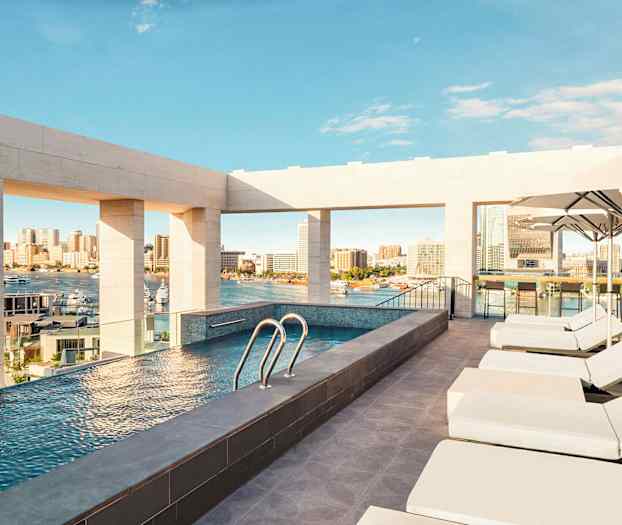 En takterrass erbjuder en pool med utsikt över en stad och hamn, omgiven av solstolar och parasoller. (AI-genererad text)