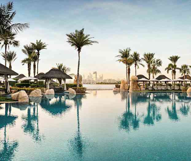 Utsikt över en pool framför resorten med palmer och parasoller. (AI-genererad text)