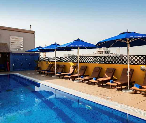 En pool med solstolar och parasoller vid sidan under en klar himmel. (AI-genererad text)