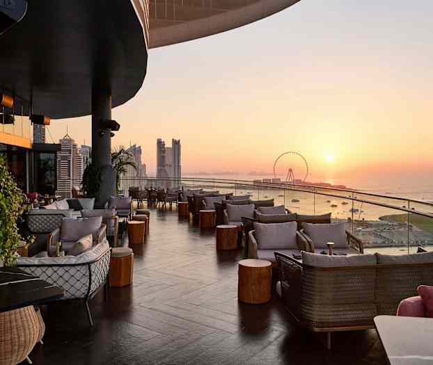 Terrass med sittplatser och utsikt över havet vid solnedgången. (AI-genererad text)