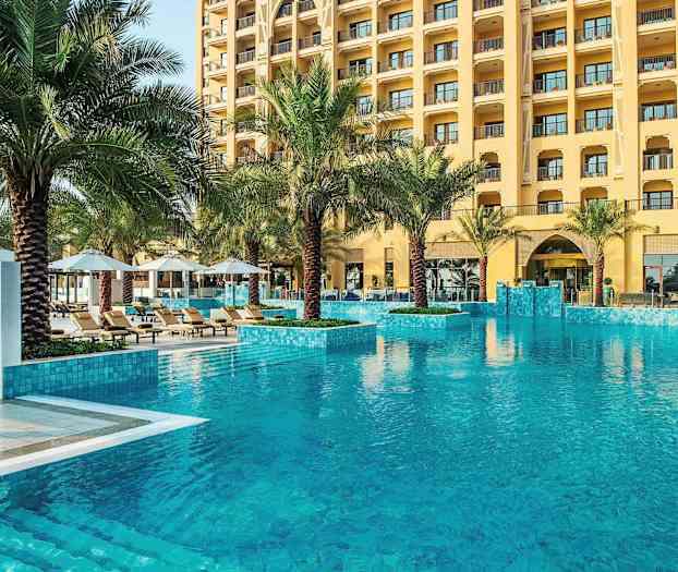 Hotellpool med klart vatten, omgiven av palmer och solstolar. (AI-genererad text)