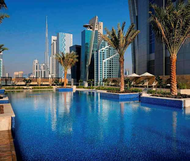 En pool omgiven av palmer med moderna byggnader i bakgrunden. (AI-genererad text)