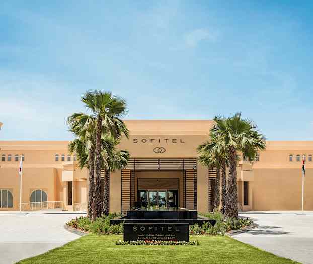 Framsidan av Sofitel-hotell med palmer och flaggor. (AI-genererad text)