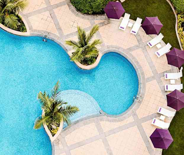 En utomhuspool med stolar och parasoller i lila färg runt omkring. (AI-genererad text)