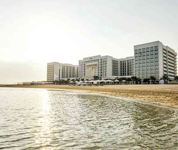 Ett stort hotellkomplex vid en strand med hav i förgrunden. (AI-genererad text)