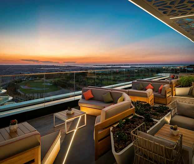 En takterrass med eleganta sittmöbler och glasräcke som erbjuder en panoramavy över landskapet i solnedgång. (AI-genererad text)