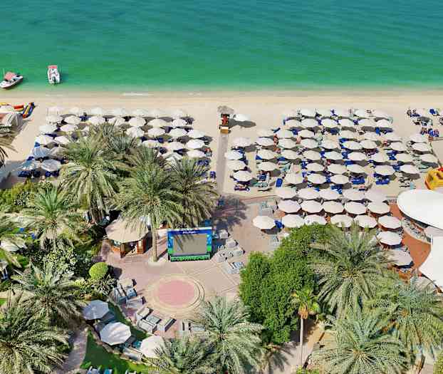 Bild av en strand med parasoller, solstolar, två båtar i vattnet samt palmträd och grönska i förgrunden. (AI-genererad text)