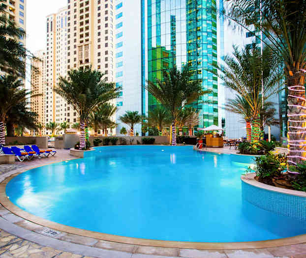 En utomhuspool omgiven av palmer med höghus i bakgrunden. (AI-genererad text)