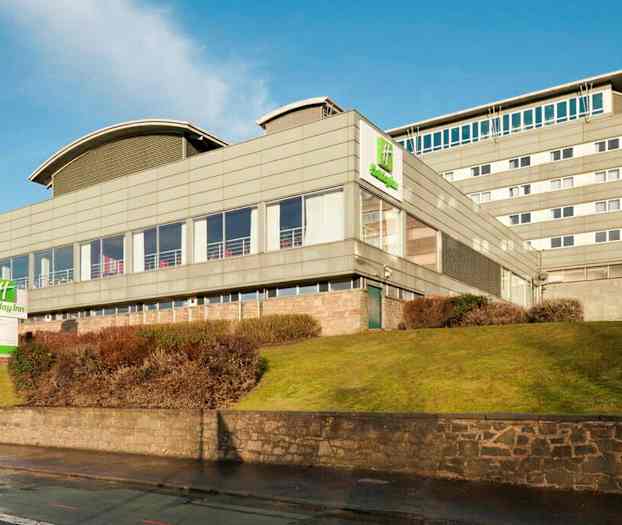 Holiday Inn-hotell i en modern byggnad med omgivande gräsmatta och buskar. (AI-genererad text)