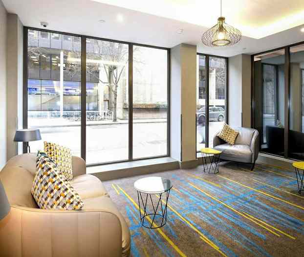 Rum med stora glasfönster, fåtöljer och små bord. (AI-genererad text)