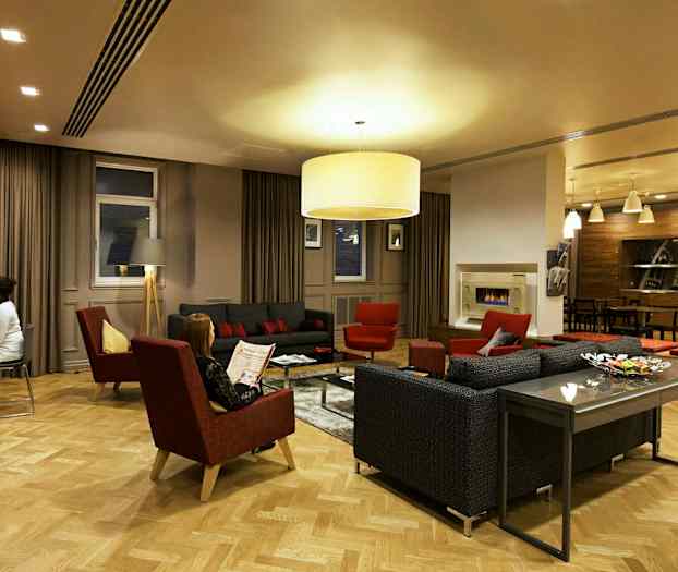 Ett elegant vardagsrum med soffor, fåtöljer och ett soffbord omgivna av varm belysning och modern inredning. (AI-genererad text)