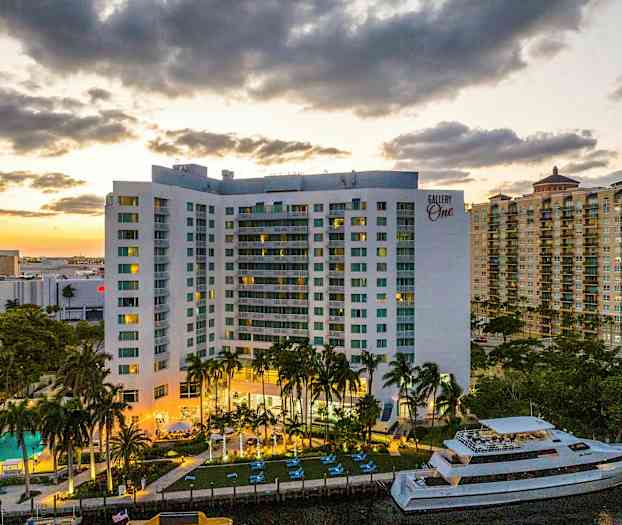 Ett flerfamiljshus med balkonger, en swimmingpool och en båt är synliga i förgrunden. Solnedgången skapar en varm bakgrund. (AI-genererad text)