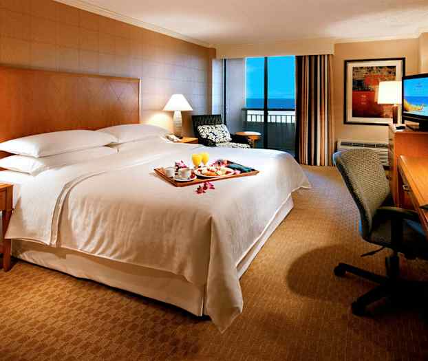 Ett sovrum i ett hotellrum med en stor säng, sidobord, skrivbord och fönster med utsikt. (AI-genererad text)