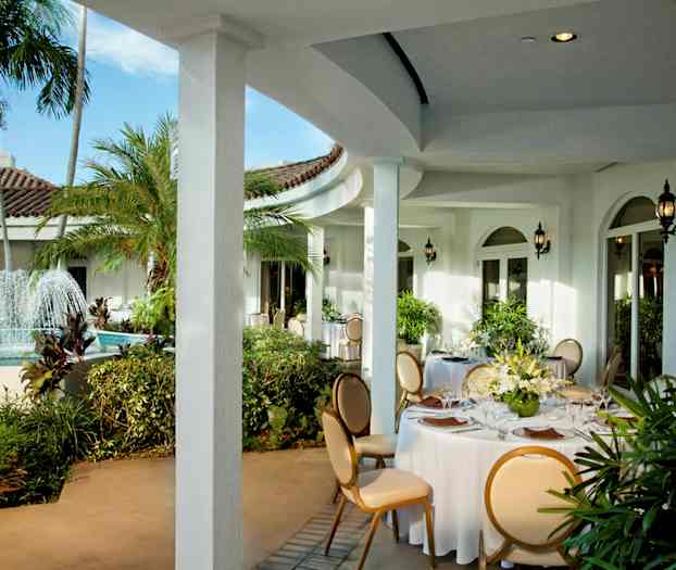 En utomhusterrass med ett fontän och runda bord dekorerade med vita dukar och blomsterarrangemang. (AI-genererad text)