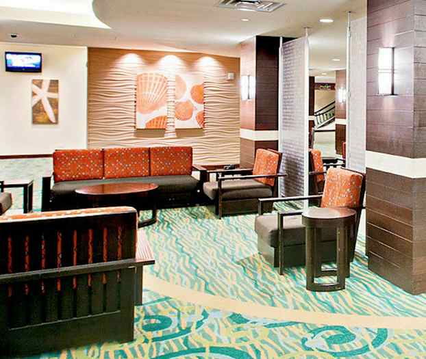 Ett väntrum med färgglad matta, flera stolar och soffor med orange tyg, samt väggdekorationer. (AI-genererad text)