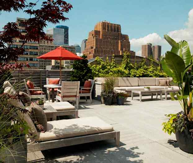 En rymlig takterrass med utemöbler, parasoll och växter. I bakgrunden syns byggnader och en klar himmel. (AI-genererad text)