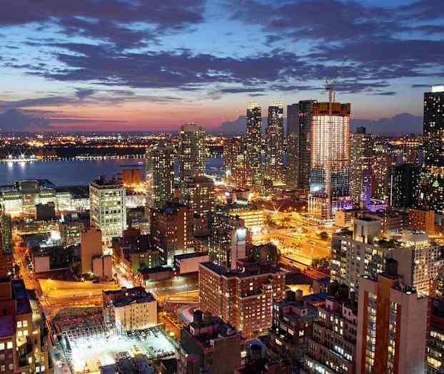 En nattlig stadsmiljö med flera upplysta byggnader och gator, med en flod i bakgrunden. (AI-genererad text)