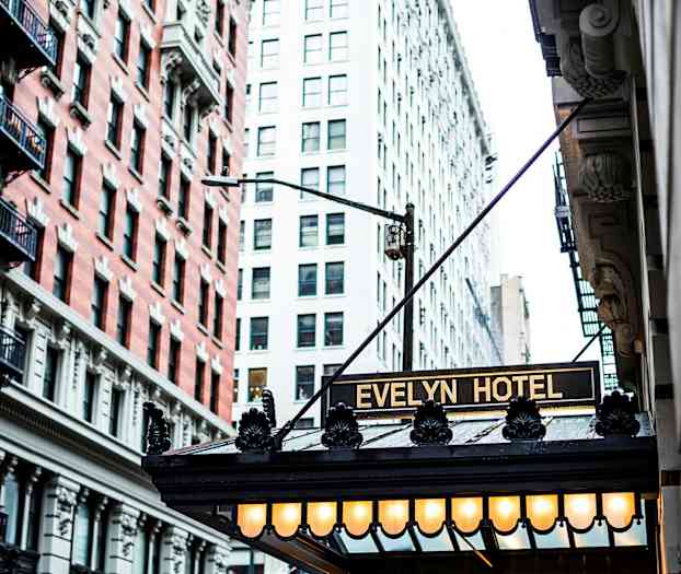 Bilden visar hotellentrén till Evelyn Hotel med en ljusskylt och fasader av byggnader runt omkring. (AI-genererad text)