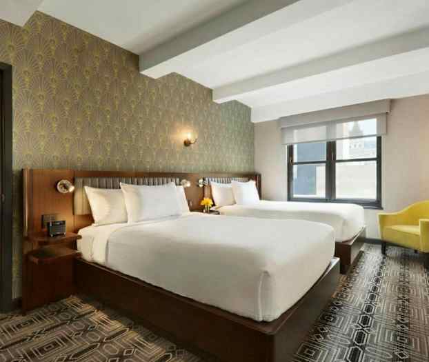 Ett hotellrum med två stora sängar, en gul fåtölj, dekorativ tapet och ett fönster. (AI-genererad text)