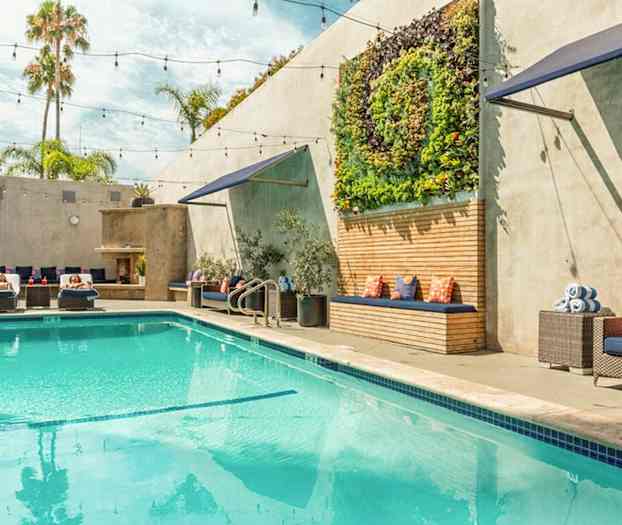 En utomhusbassäng med solstolar, gröna växter på väggen, och sittplatser med dynor. (AI-genererad text)