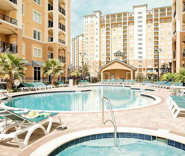 Bild av en utomhuspool omgiven av solstolar och omgärdad av byggnader med flera våningar. (AI-genererad text)